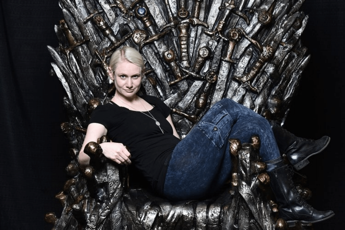 Justine lounges on the Iron Throne, legs over the arms of the chair.